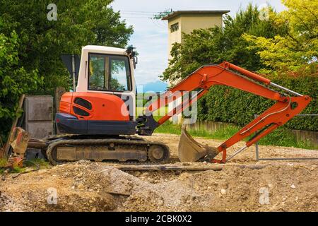 Escavatore cingolato compatto con piattaforma girevole e cingoli caterpillar continui su un cantiere di sostituzione delle fogne in Italia nord-occidentale Foto Stock