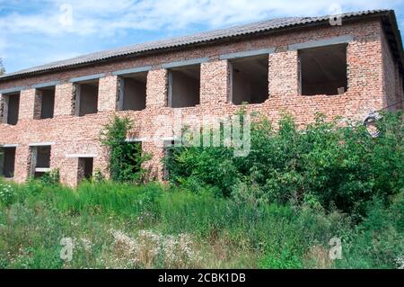 incompiuta, ma già distrutta casa a due piani di mattoni rossi con erba sopravfatta e alberi cortile Foto Stock