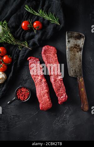 Set crudo di denver tagliato carne biologica con rosmarino vegetale e altri ingredienti vicino macellaio carne coltello intelligente per barbecue o grigliare su pietra nera Foto Stock