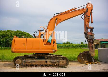 Escavatore cingolato con piattaforma girevole e continuo cingolatura caterpillar su un cantiere di sostituzione fognario a nord Italia occidentale Foto Stock