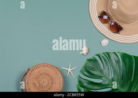 Cappello di paglia estivo, foglia di monstera tropicale, occhiali da sole, conchiglie, stelle marine su sfondo verde. Vista dall'alto, spazio copia. Foto Stock