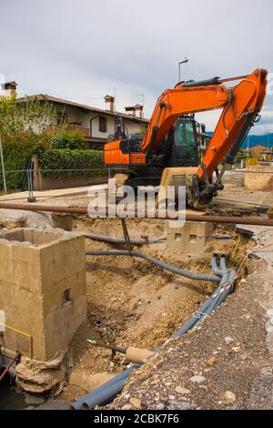 Una trincea di pozzo di fogna e un escavatore cingolato con un piattaforma rotante e cingolo caterpillar continuo su una fogna Cantiere di sostituzione in NE Italia Foto Stock