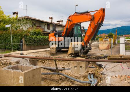 Una trincea di pozzo di fogna e un escavatore cingolato con un piattaforma rotante e cingolo caterpillar continuo su una fogna Cantiere di sostituzione in NE Italia Foto Stock