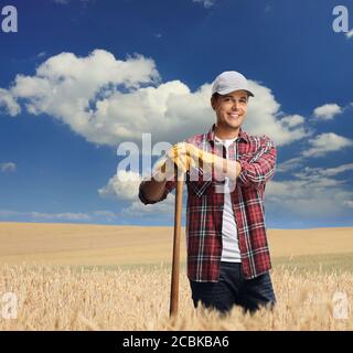 Agricoltore maschio con un attrezzo di legno in piedi in un grano e sorridendo alla telecamera Foto Stock