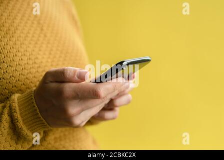 Donna in pullover giallo con smartphone. Primo piano Foto Stock