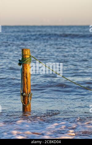 Un palo di legno o posta nelle acque poco profonde di San Ciro utilizzato per ancorare le reti di salmone dei pescatori locali, nella luce della sera Foto Stock