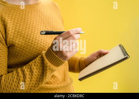 Donna in maglione di scrittura in blocco note sul giallo. Scrittura a mano Foto Stock