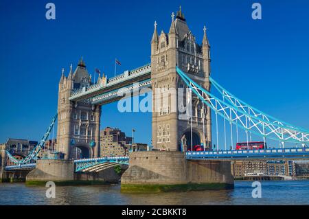 Inghilterra, Londra, Tower Bridge vista dalla riva sud del Tamigi con un iconico autobus rosso londinese che attraversa il ponte. Foto Stock