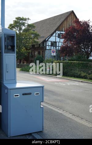 Radar foto di sicurezza in Svizzera strada vicino a una casa bianca con la recinzione di siepe verde e lampione stradale con segnaletica stradale. Foto Stock