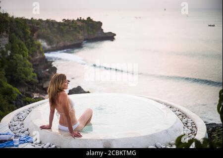 Donna seduta nella piscina termale, con vista sul mare, Balangan, Bali, Indonesia Foto Stock