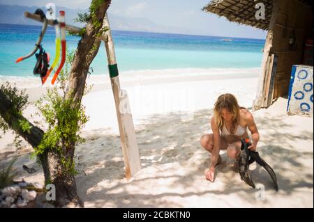 Donna accovacciata sulla sabbia, tenendo le pinne, Gili Air, Indonesia Foto Stock