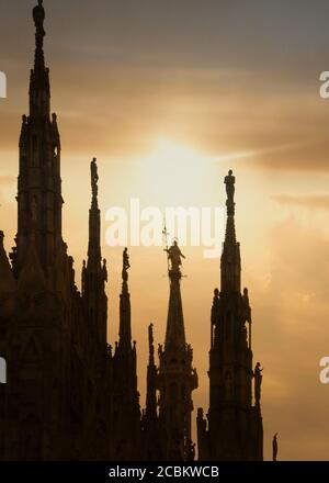 Statua della Madonna (la Madonnina) con sagome al tramonto sulla guglia più alta del Duomo di Milano Foto Stock