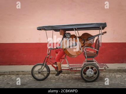 Uomo che porta il contrabbasso sul triciclo in via coloniale, Trinidad de Cuba Foto Stock