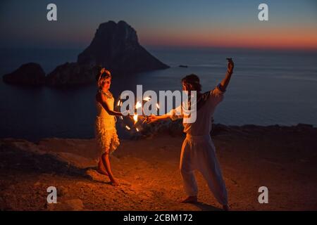 Coppia danza con fuoco tramonto, Ibiza, es Vedra rock sullo sfondo Foto Stock