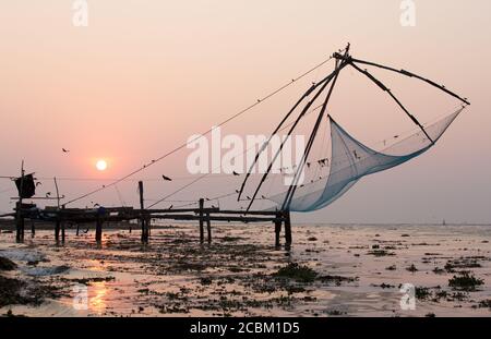 Molo e reti da pesca sulla spiaggia al tramonto, Kochi, Kerala, India Foto Stock