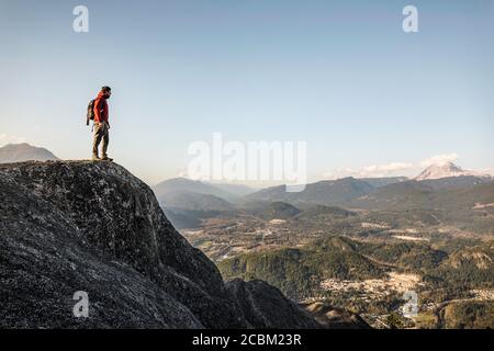 Uomo in piedi sulla montagna, guardando la vista, capo Stawamus, che domina Howe Sound Bay, Squamish, British Columbia, Canada Foto Stock