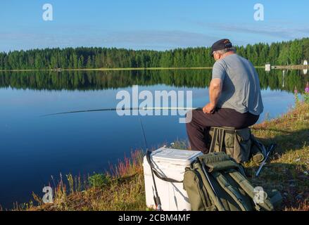 Un anziano maschio caucasico che pesca dalla riva del lago a Summer , Finlandia Foto Stock