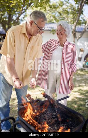 Felice coppia senior preparare barbecue in Garden.anziano uomo cucina cibo sulla griglia. Foto Stock