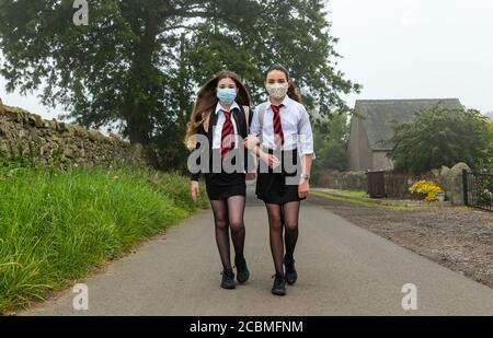 Le ragazze gemelle lasciano la casa indossando maschere per iniziare il primo giorno della scuola secondaria dopo il blocco pandemico Covid-19, Scozia, Regno Unito Foto Stock