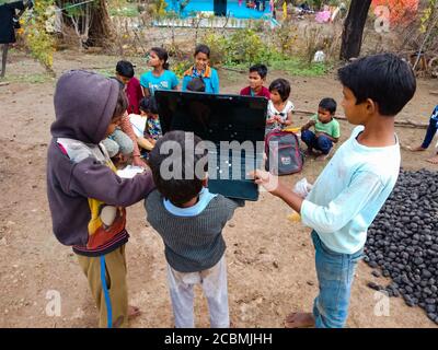 DISTRETTO KATNI, INDIA - 01 GENNAIO 2020: Tre ragazzi poveri villaggio indiano che operano il laptop con un gruppo di bambini, concetto per la consapevolezza della tecnologia digitale Foto Stock