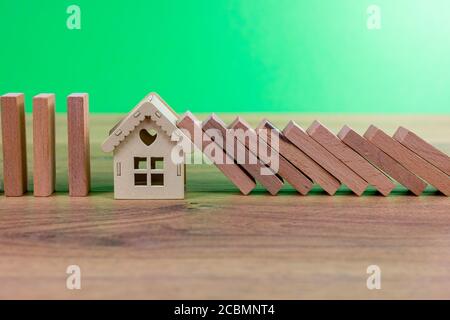 concetto di effetto domino con piastrelle di legno bloccate da casa di legno con sfondo verde Foto Stock