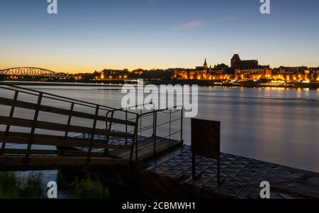 Torun visto al tramonto sul fiume Vistola. Di fronte c'è una piccola piattaforma di ormeggio Foto Stock