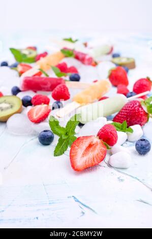 Papicle di frutta intera sane con fragole di Berries Kiwi su sfondo chiaro con un decor di ghiaccio, menta. Gustoso gelato alla frutta nella tazza. Spazio di copia. Foto Stock