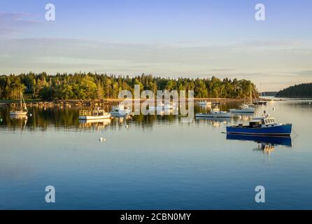 Tramonto su una baia in Pretty Marsh nel Maine. Diverse barche si siedono ancorate in acqua con il sole che getta una luce dorata su di loro Foto Stock