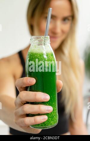 Giovane donna con bottiglia di frullato detox verde di broccoli, spinaci e cetrioli. Messa a fuoco selettiva Foto Stock