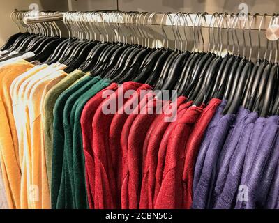 Collezione di pullover caldi multicolore appesi su una rastrelliera una boutique di moda in vendita Foto Stock