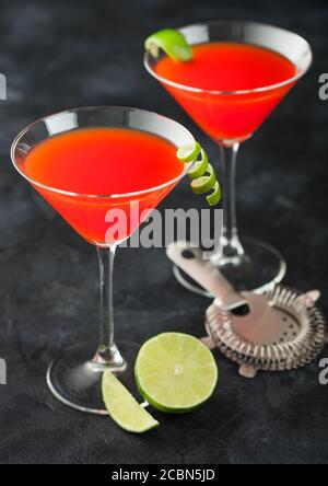 Cocktail cosmopolita in classici bicchieri di cristallo con buccia di lime e lime fresche con succhieruola su sfondo nero. Vista dall'alto Foto Stock