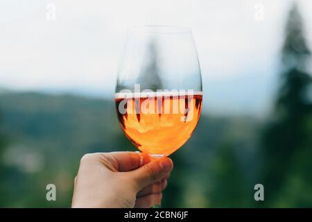 Tenere a mano delizioso cocktail arancione sullo sfondo di montagne, vacanze estive e resort. Donna che ama la bevanda aperol, festeggia all'aperto Foto Stock