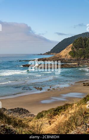 Vertical Photo - una spiaggia di sabbia e aspre colline lungo la costa dell'Oregon con una banca di nebbia appena al largo della costa. Foto Stock