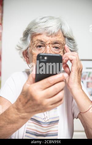 Una signora anziana che legge qualcosa sullo smartphone che ha un aspetto confuso Foto Stock