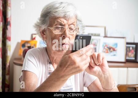 Una signora anziana che legge qualcosa sullo smartphone che ha un aspetto confuso Foto Stock