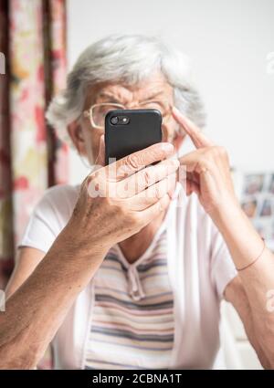 Una signora anziana che legge qualcosa sullo smartphone che ha un aspetto confuso Foto Stock
