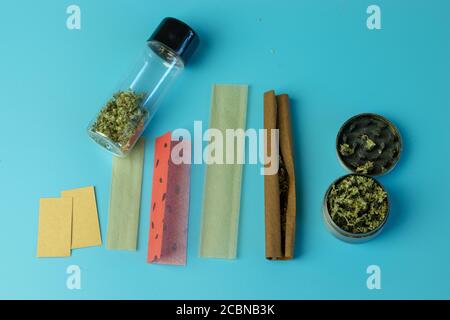 Gli accessori per fumare marijuana sono piatti su sfondo blu. Vista dall'alto di germogli di cannabis, carta articolare e smussata Foto Stock