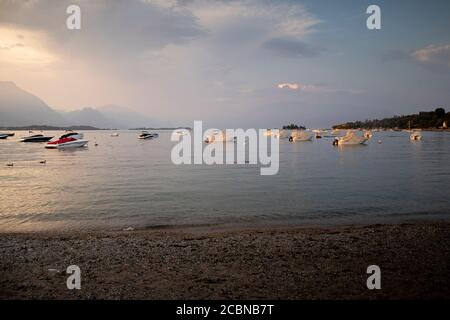 Tramonto tempestoso sulla romantica spiaggia di Manerba del Garda, Lombardia, Italia. Splendida luce dorata su imbarcazioni fisse in acque calme. Orizzontale. Foto Stock