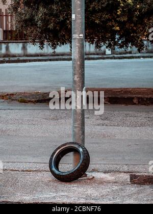 Colpo verticale di un vecchio pneumatico nei pressi di un palo in metallo arrugginito a Napoli, Italia Foto Stock