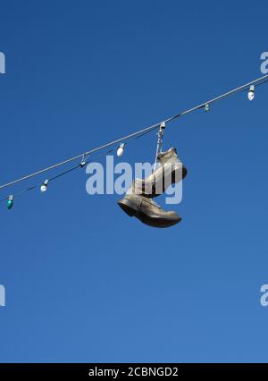 Le coppie di scarpe e scarponi pendono da un filo elettrico che corre su una strada nella zona rurale di Madrid, New Mexico USA Foto Stock