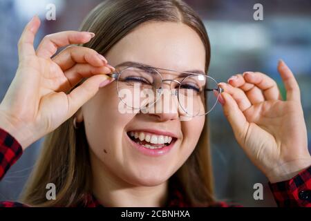 Una ragazza ipovedenti sceglie gli occhiali. Indossa una camicia e un bel sorriso. Foto Stock