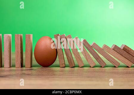 concetto di effetto domino con piastrelle di legno bloccate da uovo con sfondo verde Foto Stock