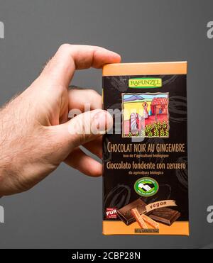 Parigi, Francia - 29 maggio 2020: Mano dell'uomo tenuta contro sfondo grigio confezione con cioccolato fondente con zenzero biologico fresco prodotto da Rapunzel Foto Stock