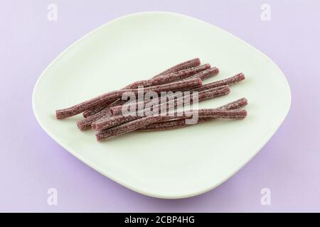 Le caramelle al mirtillo acide si attaccano su una piastra bianca per spuntini sulla lavanda sfondo Foto Stock