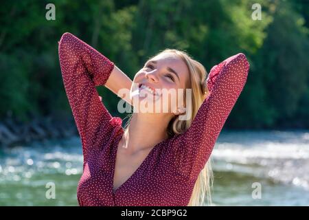 Ritratto giovane bionda all'acqua, braccia incrociate dietro la testa, felice, gioia, estate, Isar, Baviera, Germania Foto Stock