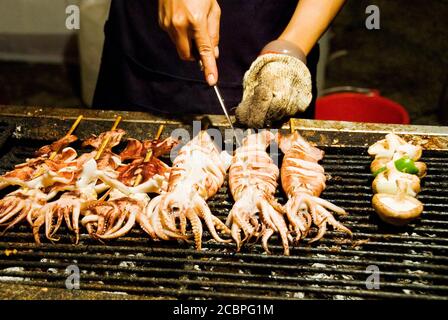 Stack di molti spiedini di calamari alla griglia nel mercato notturno. Foto Stock