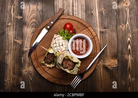 Concetto di fast food. Pane piatto con ripieno di maiale o pollo e salsa di peperoncino rosso. Burrito o tortilla serviti in ristorante o caffè. Carne tritata avvolta con pane di lavasino su fondo di legno. Foto Stock