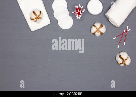 Asciugamani in spugna bianca, tamponi in cotone e boccioli con fiori di cotone su tavolo in legno grigio. Concetto di accessori per la cura della pelle in cotone con spazio per la copia Foto Stock