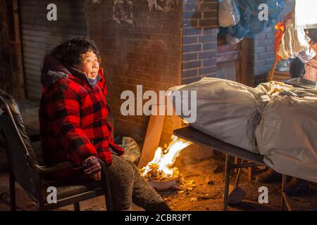 Luoyang, Provincia Henan / Cina - 3 gennaio 2016: Povera donna cinese che cerca di riscaldarsi vicino al fuoco nel quartiere della città vecchia di Luoyang Foto Stock