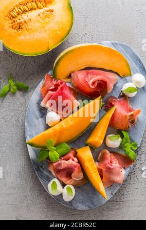 Antipasto tradizionale italiano - Prosciutto con melone di cantalupo, mozzarella, basilico e menta Foto Stock